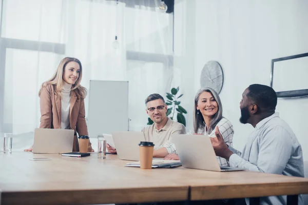 Sonrientes colegas multiculturales hablando durante la reunión en agencia creativa - foto de stock