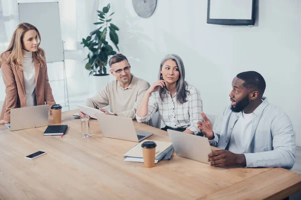 Colegas multiculturales hablando durante la reunión en la agencia creativa - foto de stock