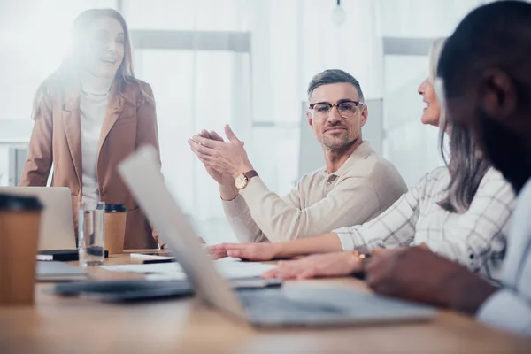 Enfoque selectivo de sonreír colegas multiculturales hablando durante la reunión en la agencia creativa - foto de stock