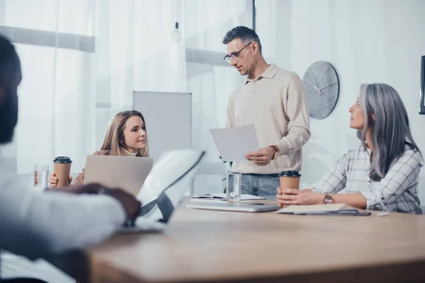 Selective focus of multicultural colleagues talking and doing paperwork in creative agency — Stock Photo