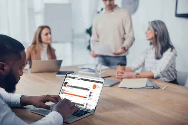 KYIV, UKRAINE - DECEMBER 6, 2019: selective focus of african american man using laptop with souncloud website and his colleagues talking on background — Stock Photo