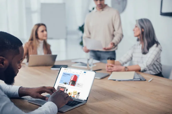 KYIV, UKRAINE - DECEMBER 6, 2019: selective focus of african american man using laptop with ebay website and his colleagues talking on background — Stock Photo