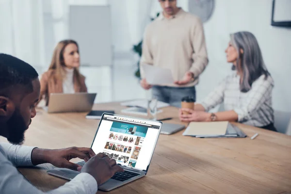 KYIV, UKRAINE - DECEMBER 6, 2019: selective focus of african american man using laptop with amazon website and his colleagues talking on background — Stock Photo