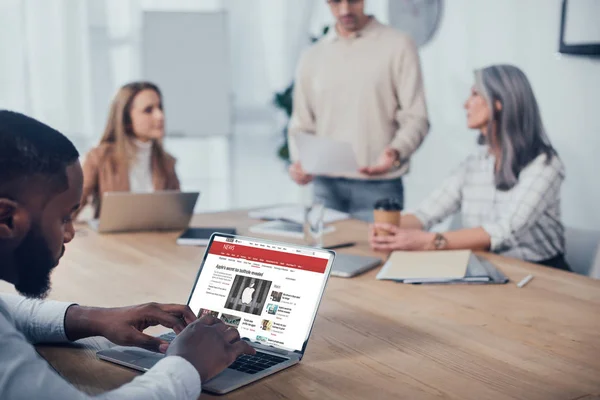 Kiew, Ukraine - 6. Dezember 2019: selektiver Fokus eines afrikanisch-amerikanischen Mannes mit Laptop mit bbc-Webseite und seinen Kollegen im Hintergrundgespräch — Stockfoto
