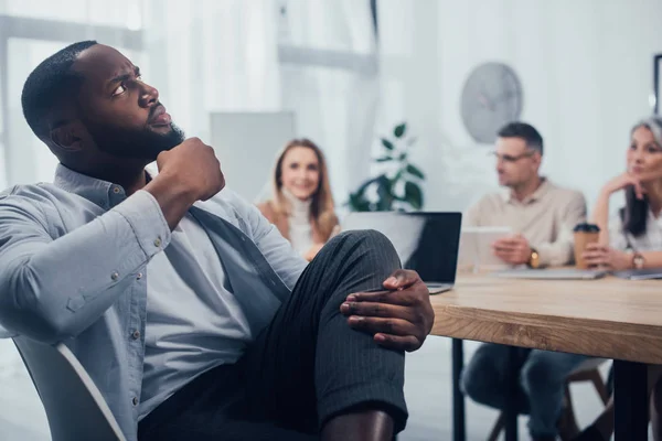 Messa a fuoco selettiva dell'uomo afroamericano pensieroso e dei suoi colleghi sullo sfondo — Foto stock