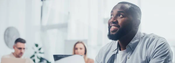 Panoramic shot of smiling african american and colleagues on background — Stock Photo