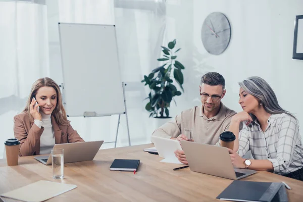 Smiling multicultural colleagues talking and using gadgets in creative agency — Stock Photo