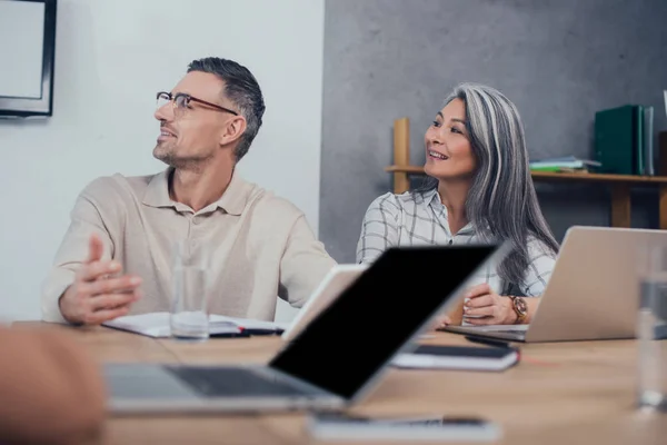 Selective focus of smiling multicultural colleagues looking away — Stock Photo