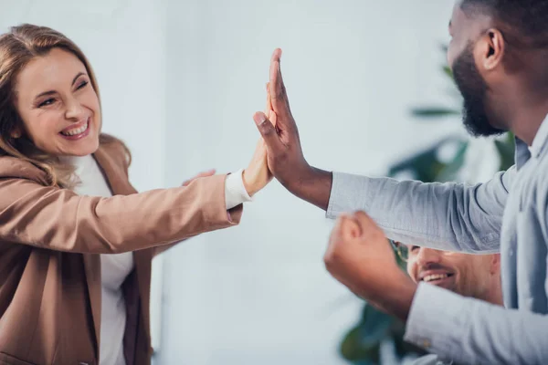 Vista recortada de sonrientes colegas multiculturales dando choca cinco en agencia creativa - foto de stock