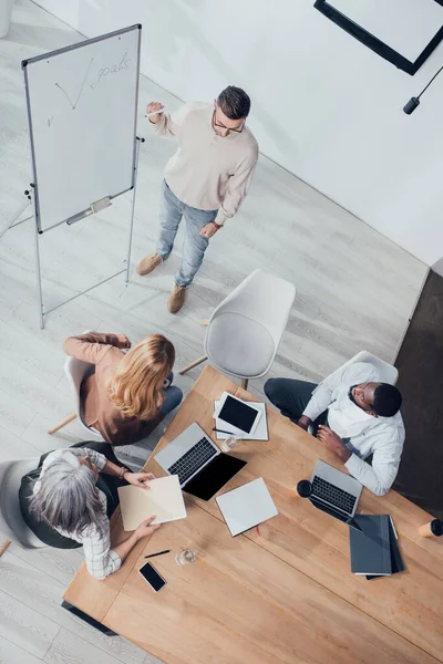 Overhead view of multicultural colleagues sitting at table and looking at businessman during presentation — Stock Photo