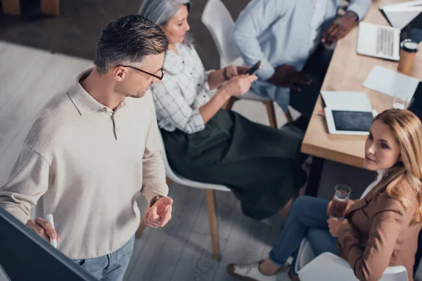 Vista de ángulo alto del hombre de negocios mostrando signo de idea y mirando a colega durante la presentación - foto de stock