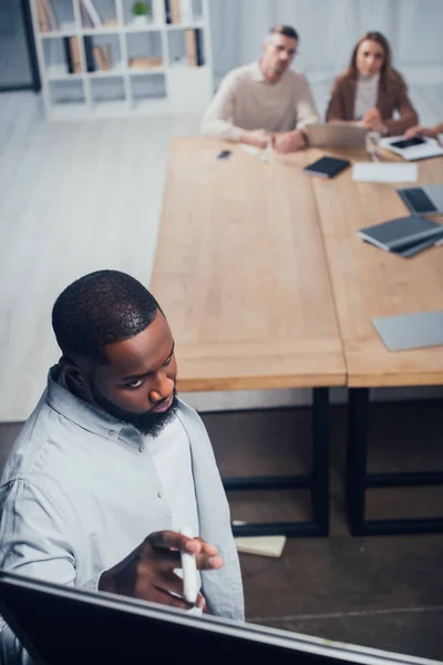 Selektiver Fokus eines afrikanisch-amerikanischen Geschäftsmannes, der bei der Präsentation für Kollegen mit Filzstift auf Flipchart zeigt — Stockfoto