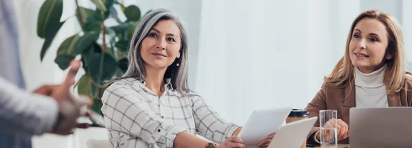 Panoramic shot of smiling multicultural colleagues looking at african american businessman — Stock Photo