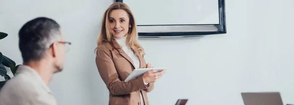 Tiro panorâmico de mulher de negócios sorridente com tablet digital olhando para seu colega — Fotografia de Stock