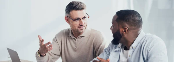 Panoramic shot of smiling multicultural colleagues talking in creative agency — Stock Photo
