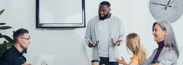 Plano panorámico del hombre de negocios afroamericano hablando con colegas multiculturales sonrientes - foto de stock