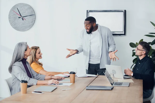 Felice uomo d'affari afroamericano con le mani tese parlando con i suoi colleghi — Foto stock