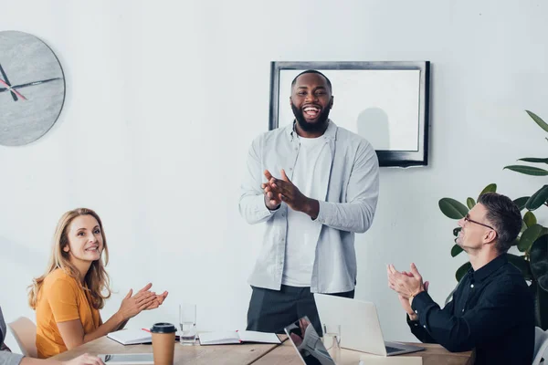 Sorridenti colleghi multiculturali applaudono e guardano la macchina fotografica nell'agenzia creativa — Foto stock