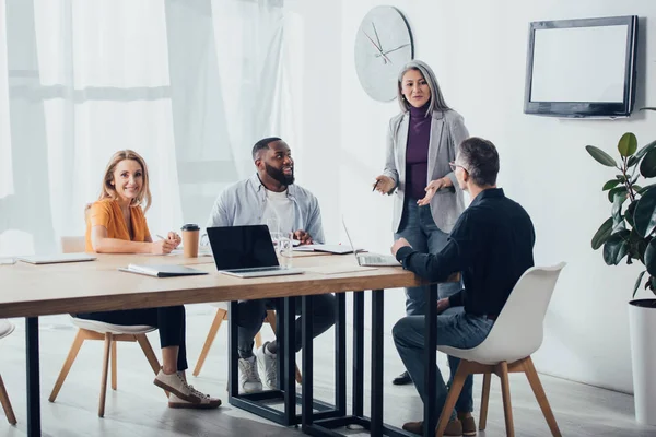 Smiling multicultural colleagues talking with asian businesswoman — Stock Photo