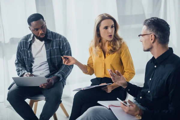 Colegas multiculturales sentados y hablando en agencia creativa - foto de stock