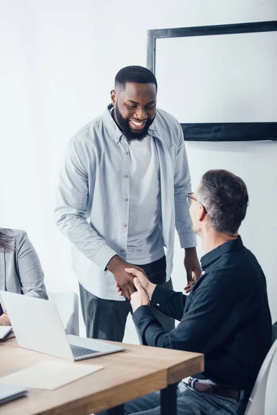 Sonriente hombre de negocios afroamericano dándole la mano a su colega - foto de stock