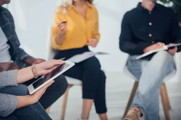 Vista recortada de la mujer sosteniendo tableta digital y sentado cerca de colegas multiculturales - foto de stock