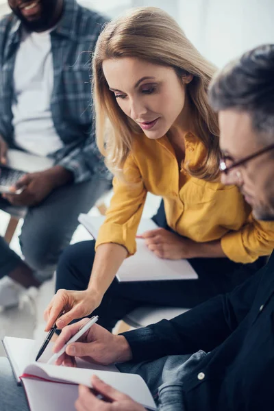 Selective focus of businesswoman pointing with pen at notebook with her colleague — Stock Photo