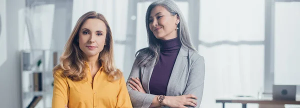 Panorâmica tiro de sorridente asiático empresária com cruzado braços olhando para ela colega — Fotografia de Stock