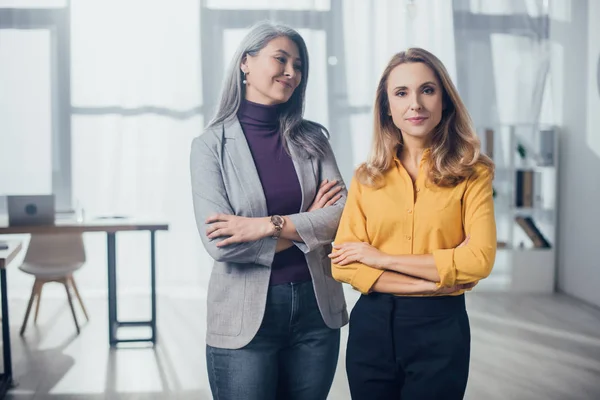 Sonrientes colegas multiculturales con brazos cruzados en agencia creativa - foto de stock