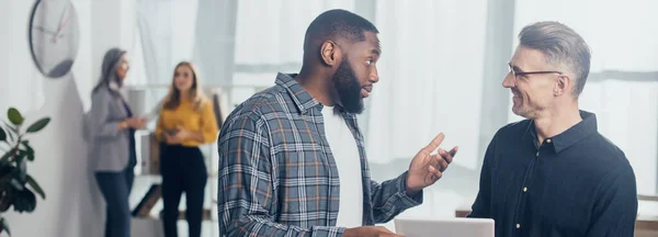 Foto panorâmica do empresário afro-americano conversando com seu colega sorridente com tablet digital — Fotografia de Stock