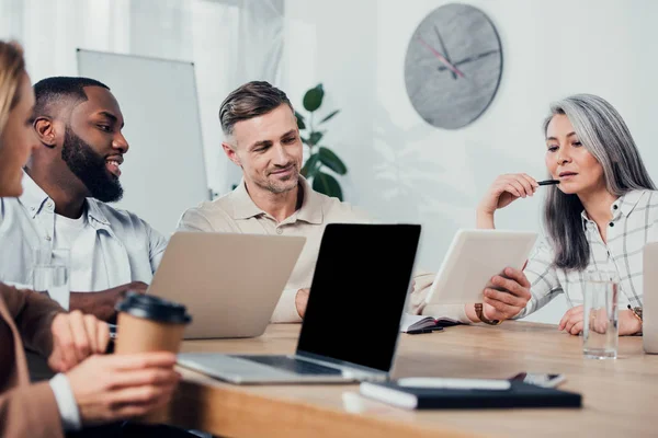 Multicultural colleagues sitting at table and looking at digital tablet — Stock Photo