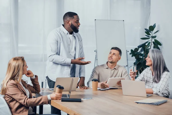 Мультикультурні колеги сидять за столом і розмовляють з афроамериканським бізнесменом — стокове фото