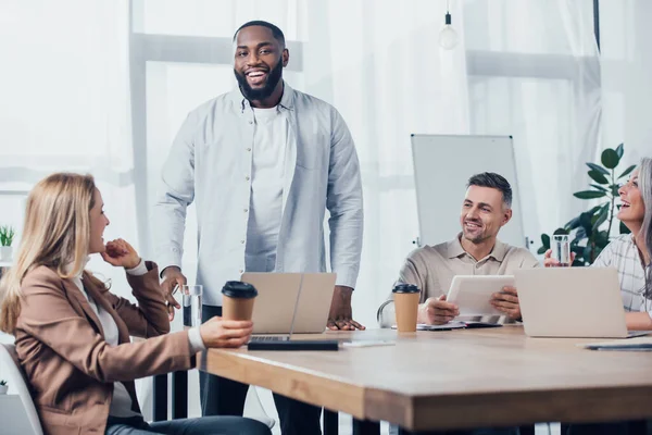 Multicultural colleagues smiling and sitting at table in creative agency — Stock Photo