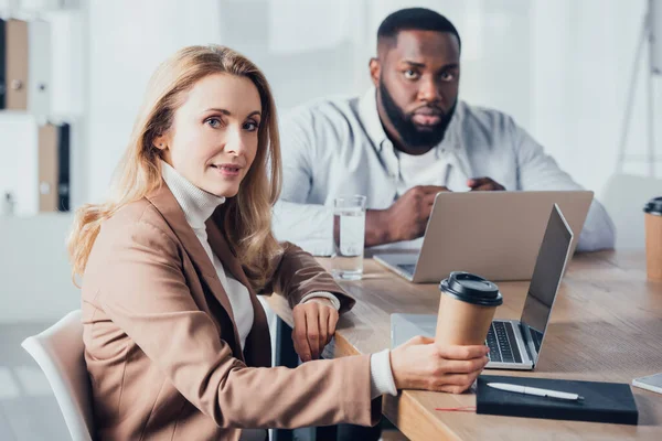 Colegas multiculturales sentados en la mesa y mirando a la cámara - foto de stock