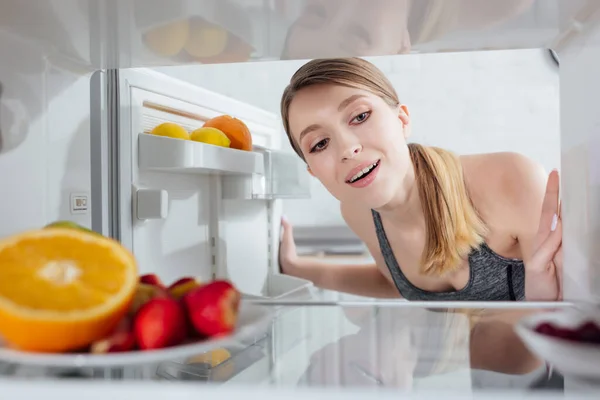 Messa a fuoco selettiva di donna allegra guardando frutta in frigorifero — Foto stock