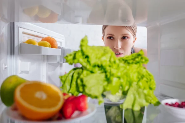 Messa a fuoco selettiva di donna attraente guardando frutta in frigorifero — Foto stock