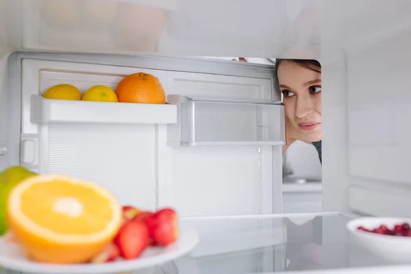 Selective focus of girl looking at fruits in fridge — Stock Photo