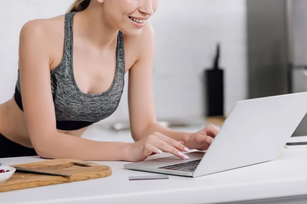 Cropped view of cheerful girl typing on laptop keyboard near credit card — Stock Photo