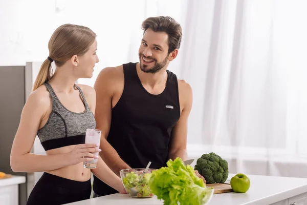 Happy man cooking near woman with glass of smoothie in kitchen — Stock Photo