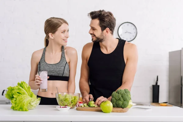 Uomo felice cucina vicino alla ragazza con un bicchiere di frullato in cucina — Foto stock