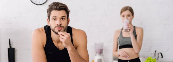 Plan panoramique de bel homme regardant la caméra près de la femme buvant smoothie — Photo de stock