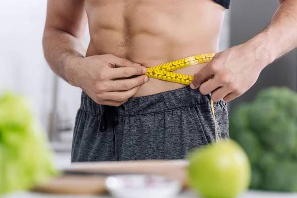 Vista cortada do homem sem camisa medir a cintura perto de alimentos nutritivos — Fotografia de Stock