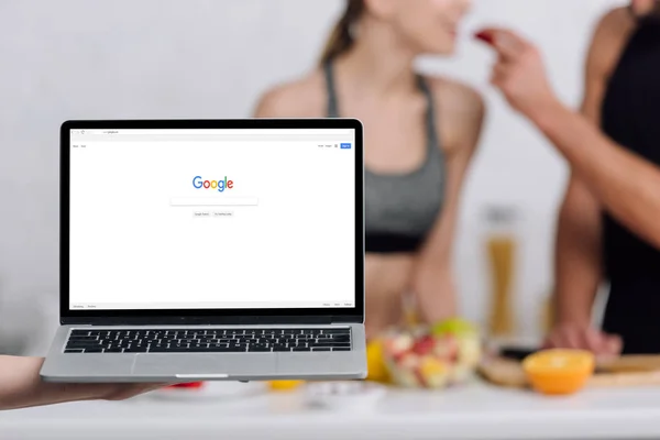 KYIV, UCRANIA - 28 DE DICIEMBRE de 2019: enfoque selectivo de la computadora portátil con google sitio web cerca de pareja en la cocina - foto de stock