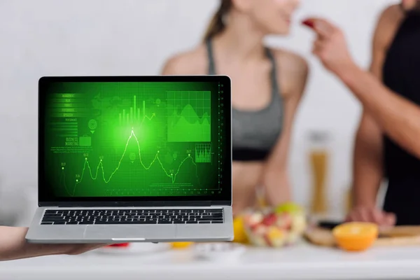 Selective focus of laptop with graphs on screen near couple in kitchen — Stock Photo