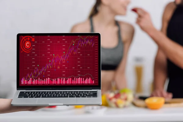 Selective focus of laptop with graphs on screen near man and woman in kitchen — Stock Photo