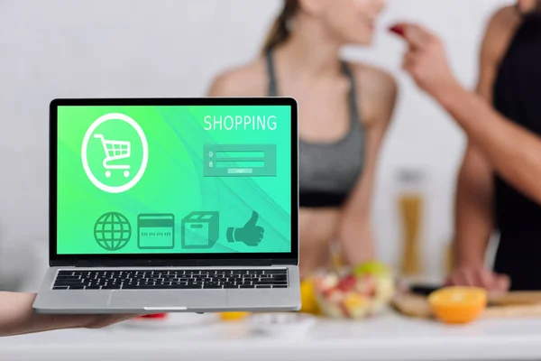 Selective focus of laptop with shopping website on screen near couple in kitchen — Stock Photo