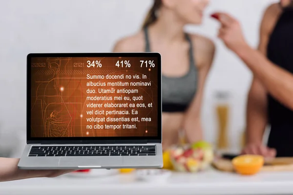 Selective focus of laptop with health website on screen near couple in kitchen — Stock Photo