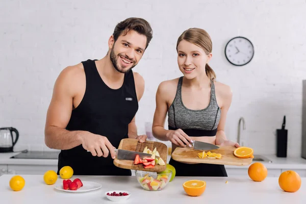 Hombre feliz y mujer alegre cocinar ensalada de frutas - foto de stock