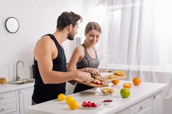 Hombre feliz y mujer alegre preparando ensalada de frutas - foto de stock