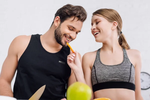 Foco seletivo de menina feliz alimentando o homem alegre com laranja fatiada — Fotografia de Stock